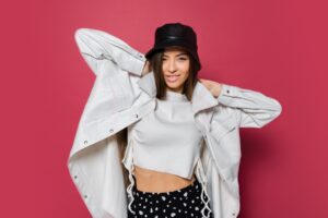 happy-cute-woman-holding-hairs-pink-background-happy-female-white-jacket-black-trendy-panama-posing-studio_273443-4043